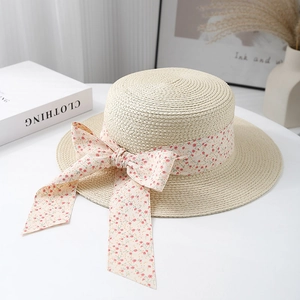 Flat top straw boater hat with pink floral ribbon and bow on a white desk