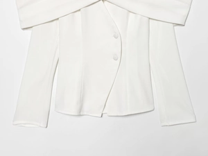 Detail of white off-shoulder long sleeve blazer featuring unique curved button placket