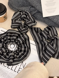 Close-up of black and white striped satin scrunchies arranged with lifestyle props