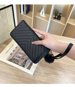 Detail of black V-quilted long leather wallet with matching wristlet and plush pompom charm
