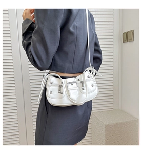 Chic white crossbody bag detail with silver studs and buckles worn by a model