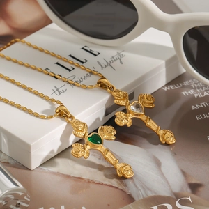 Pendentif croix rétro avec pierre en cœur et détail de rose sur une boîte blanche