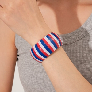 Detail showing a wide striped resin cuff bracelet with red, white, and blue diagonal patterns