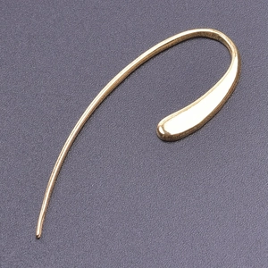 Macro view of minimalist golden curved earring with a sleek droplet tip on textured surface