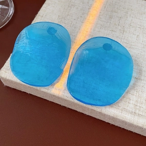 Macro view of blue translucent irregular acrylic earring pieces with fine texture on linen