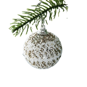 Sparkling white and gold Christmas ball ornament hanging on a green pine branch