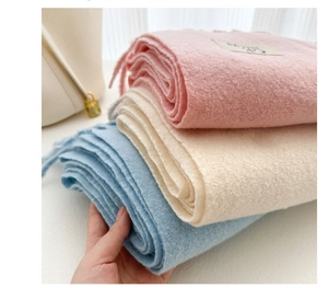 Close-up of soft pink, cream, and blue wool blend scarves held by hand to show texture