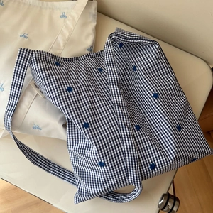 Détail d'un sac en coton à carreaux bleu et blanc avec broderie de fleurs et étiquette