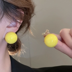 Close-up of yellow spherical stud earrings showing smooth glossy finish and earring posts
