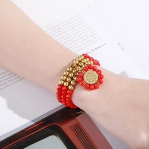 Close-up of layered red beaded bracelet with golden coin pendant and faceted glass charms