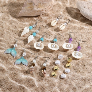 Flat lay of ocean-themed earrings with shells and pearls on beach sand background