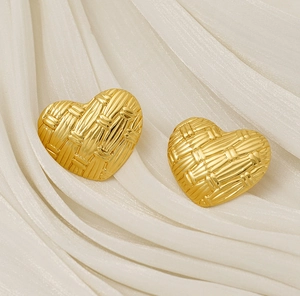 Detailed view of gold woven heart earrings on white silk fabric with elegant metallic texture