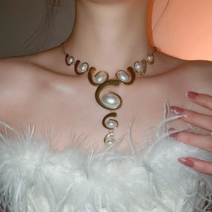 Close-up of golden asymmetric pearl necklace with oval charms on model in elegant light