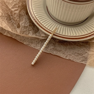 Close-up of golden metal hair clip featuring a row of elegant white pearls on ceramic