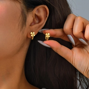 Detailed close-up of delicate golden flower-shaped hoop earrings worn by a model