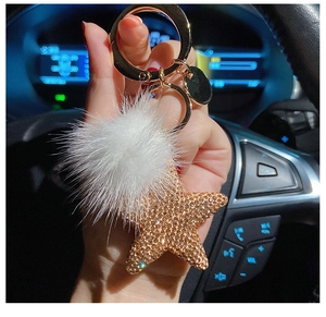Star-shaped rhinestone keychain with a white faux fur pompom shown inside a car cabin