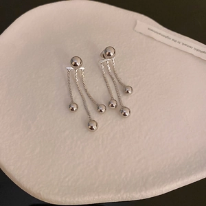 Silver drop earrings with metal bead and tassel chain design on a white textured tray