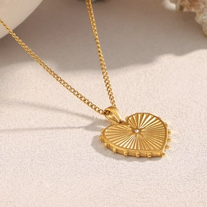 Detail of 18K gold heart pendant with radial texture and sparkling center zircon