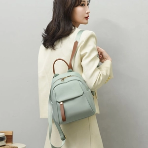 Dettaglio zaino verde chiaro con spallacci in finta pelle marrone su blazer beige chiaro