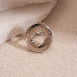 Detail of minimalist silver hollow circular ring on a textured sandy stone background