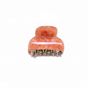 Detailed view of small peach marble acetate hair claw with silver metal teeth on white background