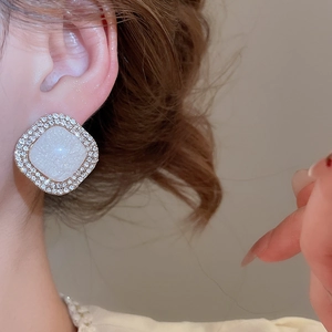 Close-up of elegant champagne gold square earrings with white stones worn by a model