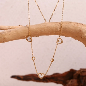 Detail view of a gold-plated necklace with three shell hearts and round diamonds on wood