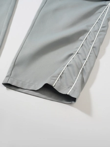 Detail of grey techwear trousers featuring parallel white side stripes and clean hem stitching