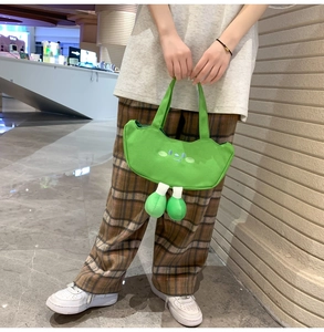 Close-up of green canvas tote bag featuring cartoon embroidery and plush ball charms