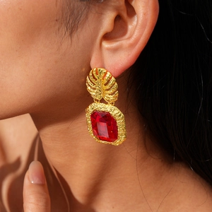 Close-up of vintage gold leaf earrings with faceted red square gemstones on a model