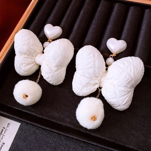 Detail of white bow earrings with heart pearl accents and soft fluffy pom pom drops