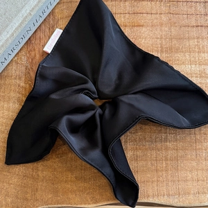 Detail of a large black satin bow scrunchie with silky texture on light wood background