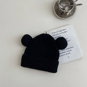 Detailed view of black ribbed knit beanie with cute double pompoms on a clean white background