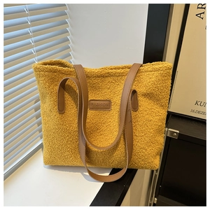 Detail of yellow plush tote bag featuring leather handles and a brown fashion patch