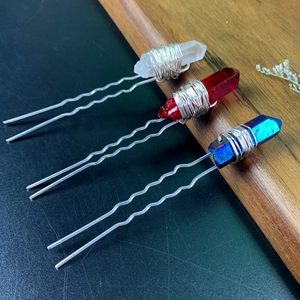 Detailed view of U-shaped hair pins with blue red and white crystals on wood