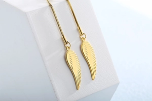 Detailed view of golden angel wing earrings with delicate snake chains on white stone