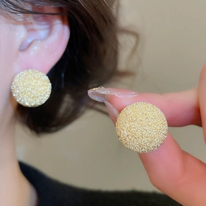 Detail view of round gold stud earrings with textured frosted finish on model's ear