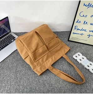 Top-down view of a large brown canvas tote bag with dual front pockets on grey felt