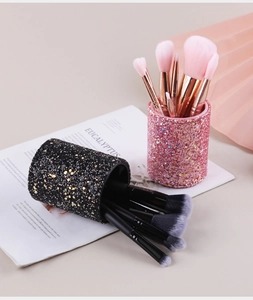 Close-up of glitter makeup brush holders in black and pink with rose gold brushes