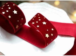 Detail of burgundy velvet ribbon with gold star print on white plate for Christmas