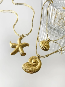 Detailed macro view of starfish and nautilus shell charms on gold plated necklaces