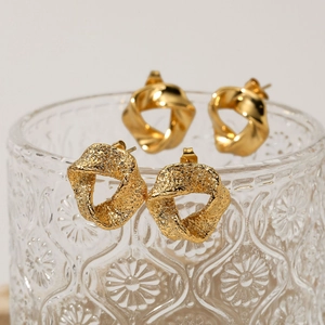 Golden geometric textured and twisted earrings displayed on elegant glass rim