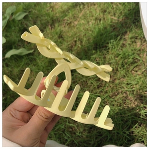 Detail view of a matte pale yellow claw clip held by hand against a natural lawn background