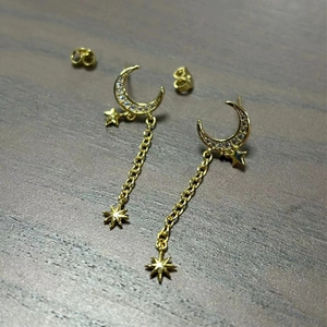 Macro detail of gold star and crescent moon tassel earrings with zircon on wood surface