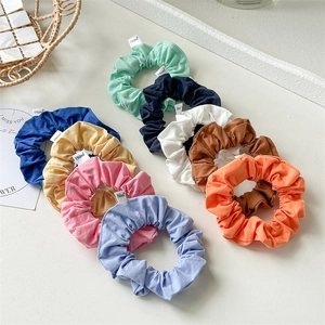 Flat lay of nine colorful cotton scrunchies set on a minimalist white surface with decor