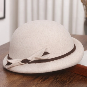 Detail of wool beret showing beige felt texture with brown ribbon and bow on wood table