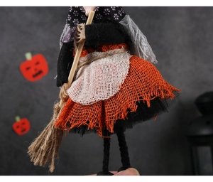 Detail of a handmade Halloween witch doll with orange burlap skirt and wooden broom decoration