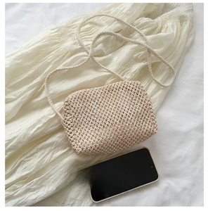 Straw woven crossbody bag size comparison with smartphone on soft white fabric background