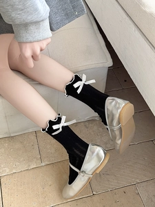 Close-up of black mid-calf socks with white ruffle trim and bows paired with silver shoes