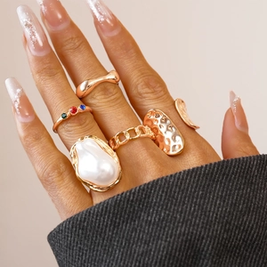 Close-up of gold geometric rings set with pearls and colorful gemstones on a model hand